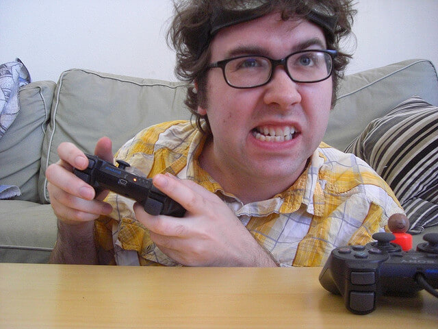 A man makes an aggressive face as he plays a playstation to represent video game addiction