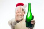 A man in a Santa Claus hat saying no by returning a green bottle of wine